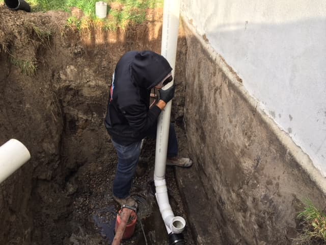 Une personne tient un assemblage de tuyau de drain français dans ses mains près d'une fondation