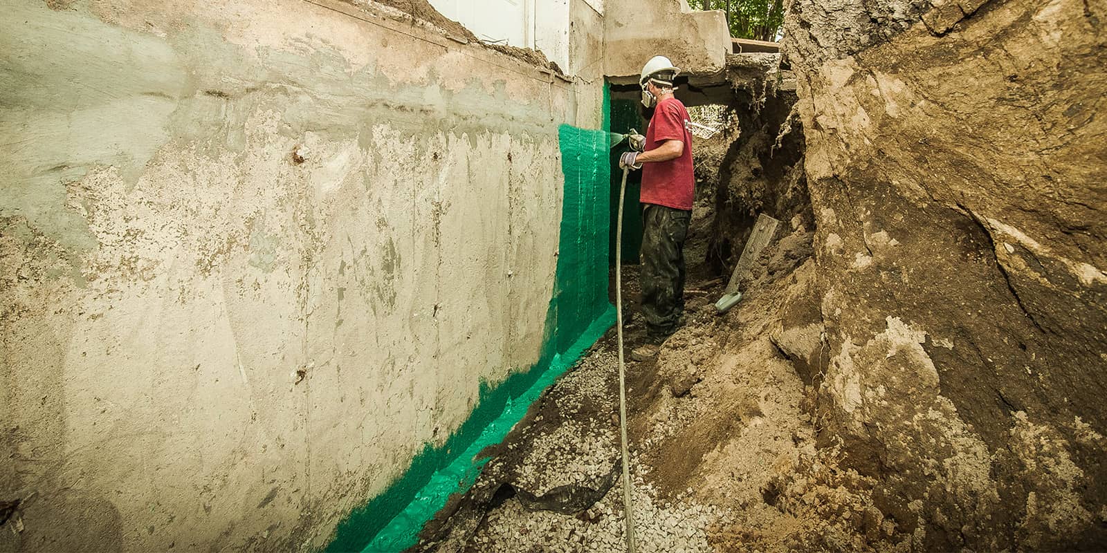 Travailleur appliquant une membrane de caoutchouc verte sur la fondation de béton d'une maison